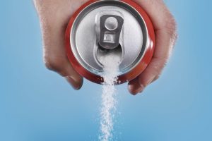 hand holding soda can pouring a crazy amount of sugar in metaphor of sugar content of a refresh drink isolated on blue background in healthy nutrition, diet and sweet addiction concept