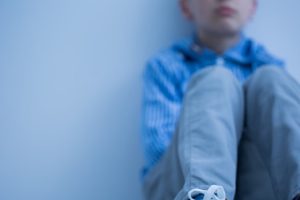Sad boy in sneakers with asperger's syndrome sits alone in his room