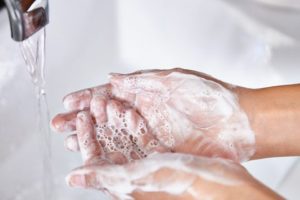 Woman washing her hands at the kitchen sink. There are vegetables out of focus in the background.